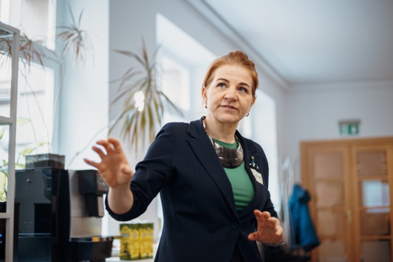 Darbnīcas vadītāja runā un žestikulē prezentācijas laikā.