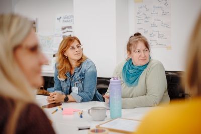 Divas darbnīcas dalībnieces klausās grupas diskusiju pie galda.
